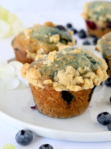A white plate with a muffin and blueberries sprinkled around.