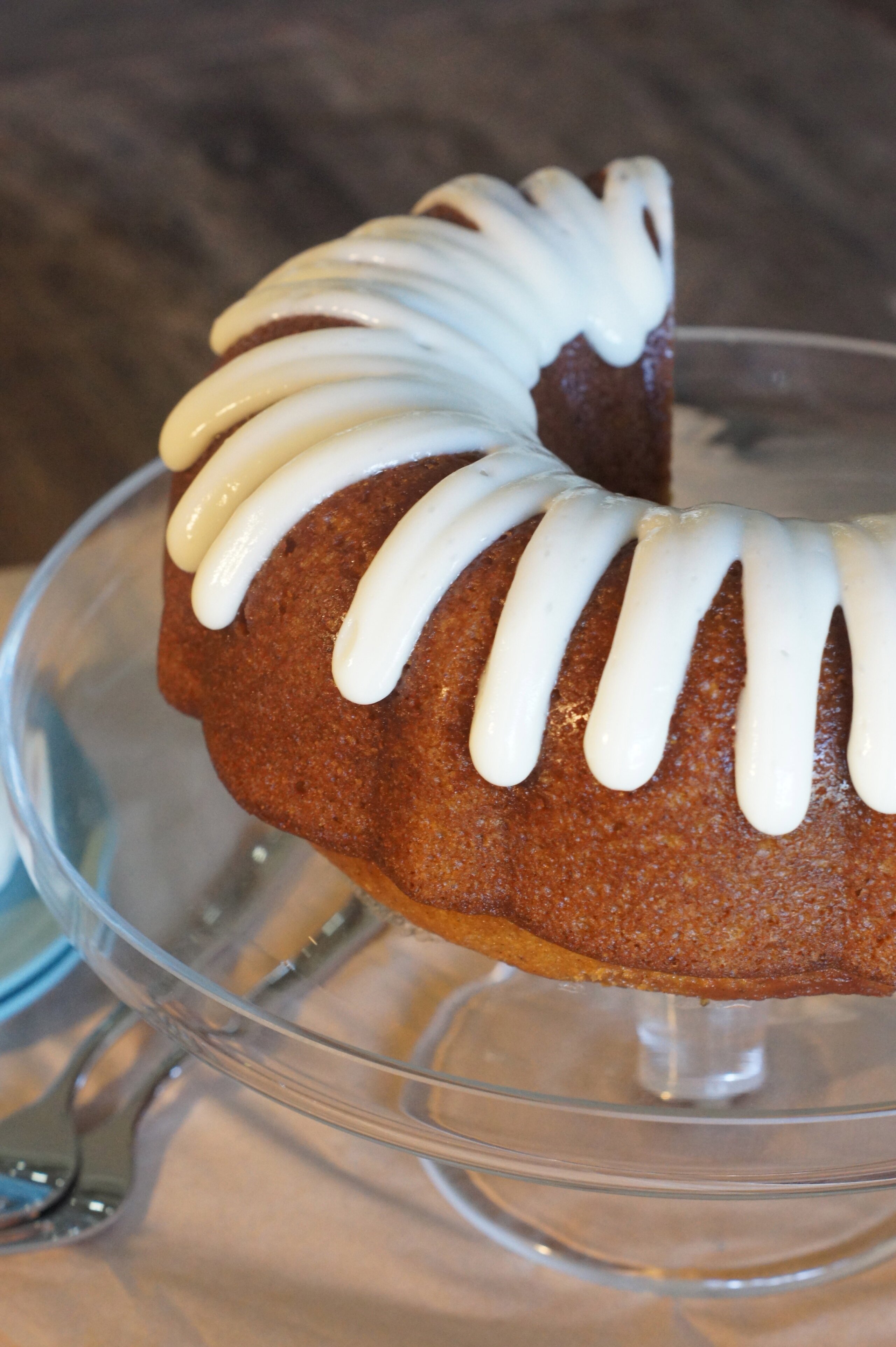A glazed pumpkin ginger bundt cake sitting on a glass cake stand, with a slice cut out