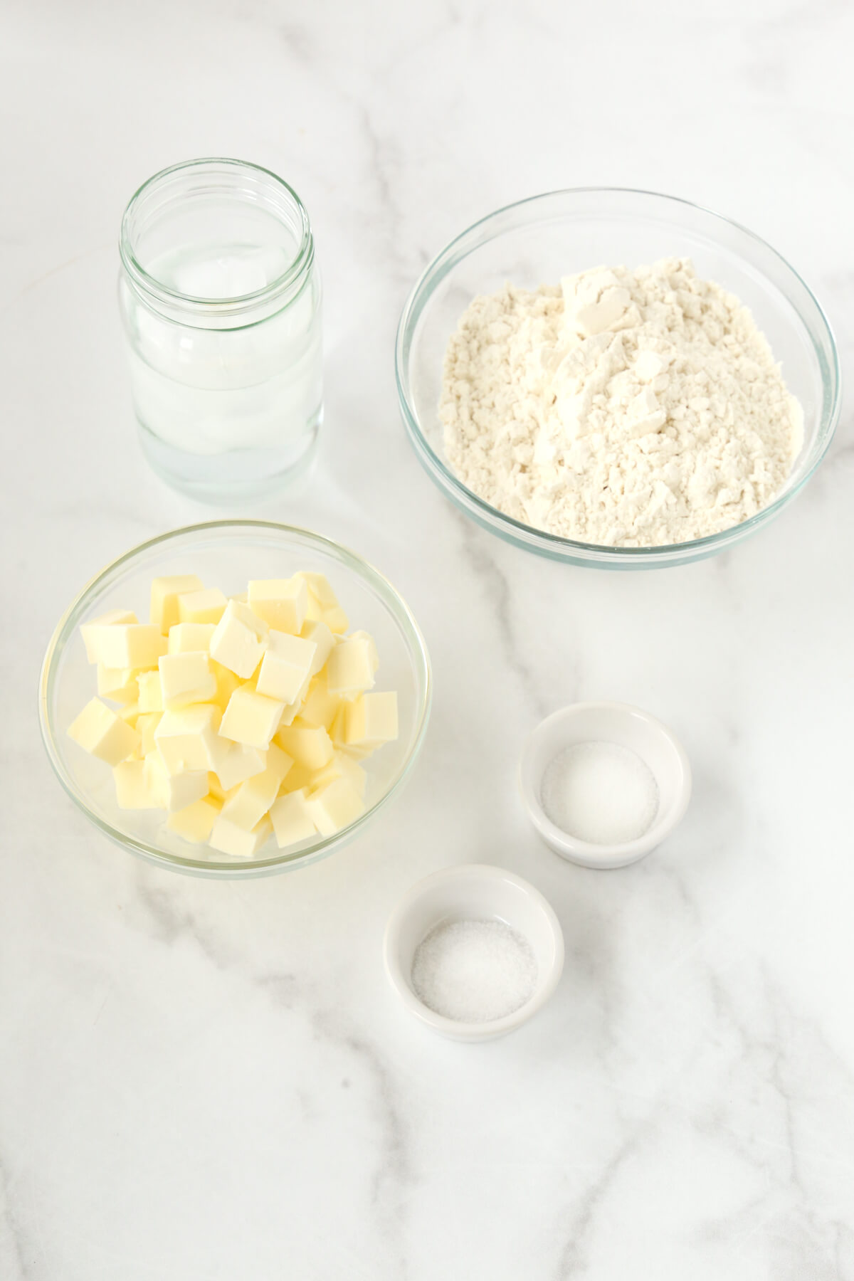 Bowls of flour, sugar, salt, cubed butter and a jar of ice cold water.  