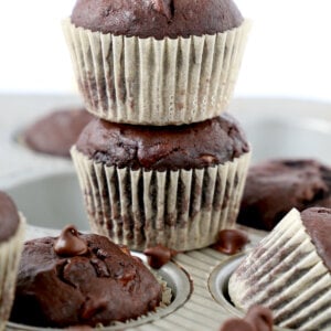 Two chocolate muffins stacked on top of each other sitting on a muffin pan.