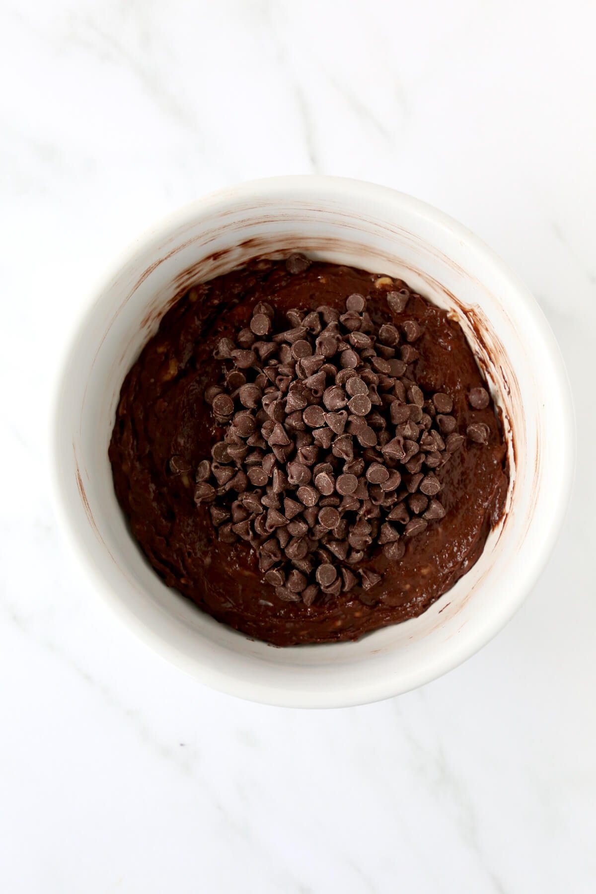 A bowl with brown muffin batter and chocolate chips on top. 