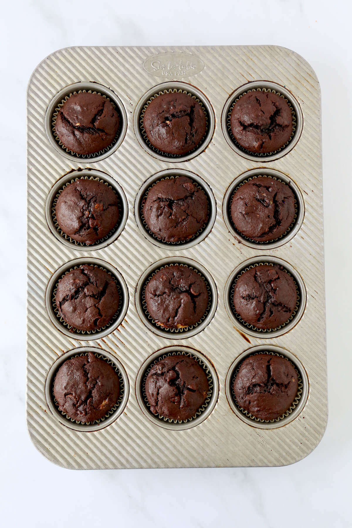Twelve baked chocolate muffins in a muffin pan.  