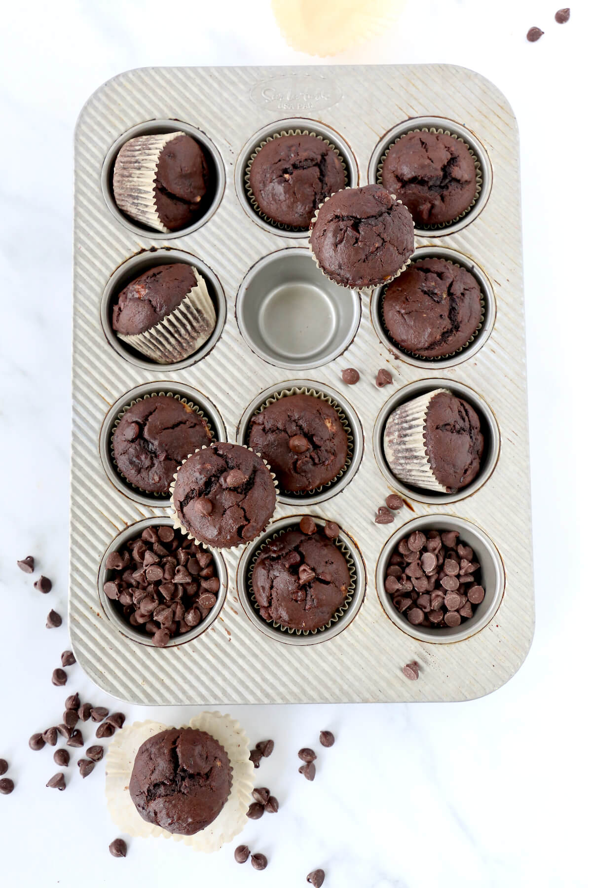 A muffin pan filled with chocolate muffins and chocolate chips.  