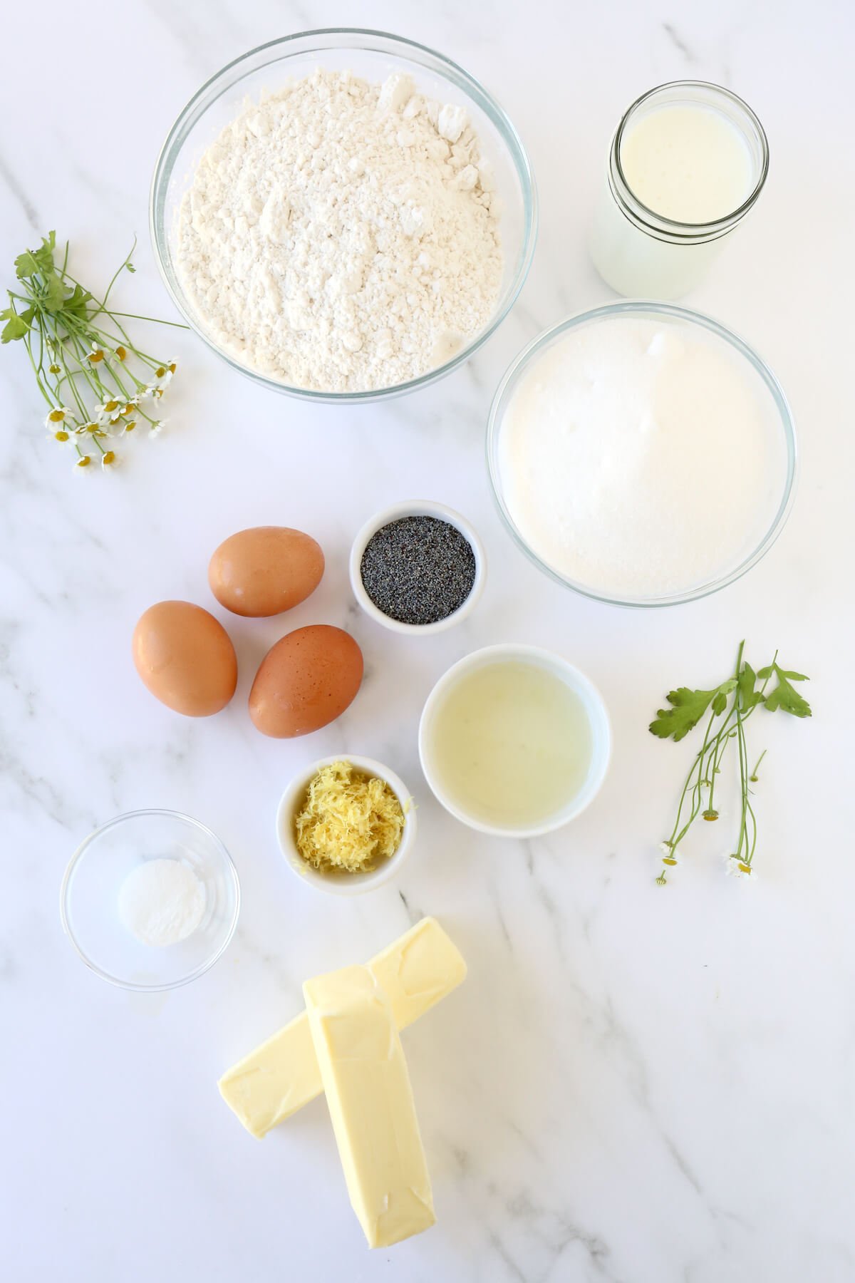 Bowls of flour, sugar, poppy seeds, lemon juice, lemon zest, eggs and butter.