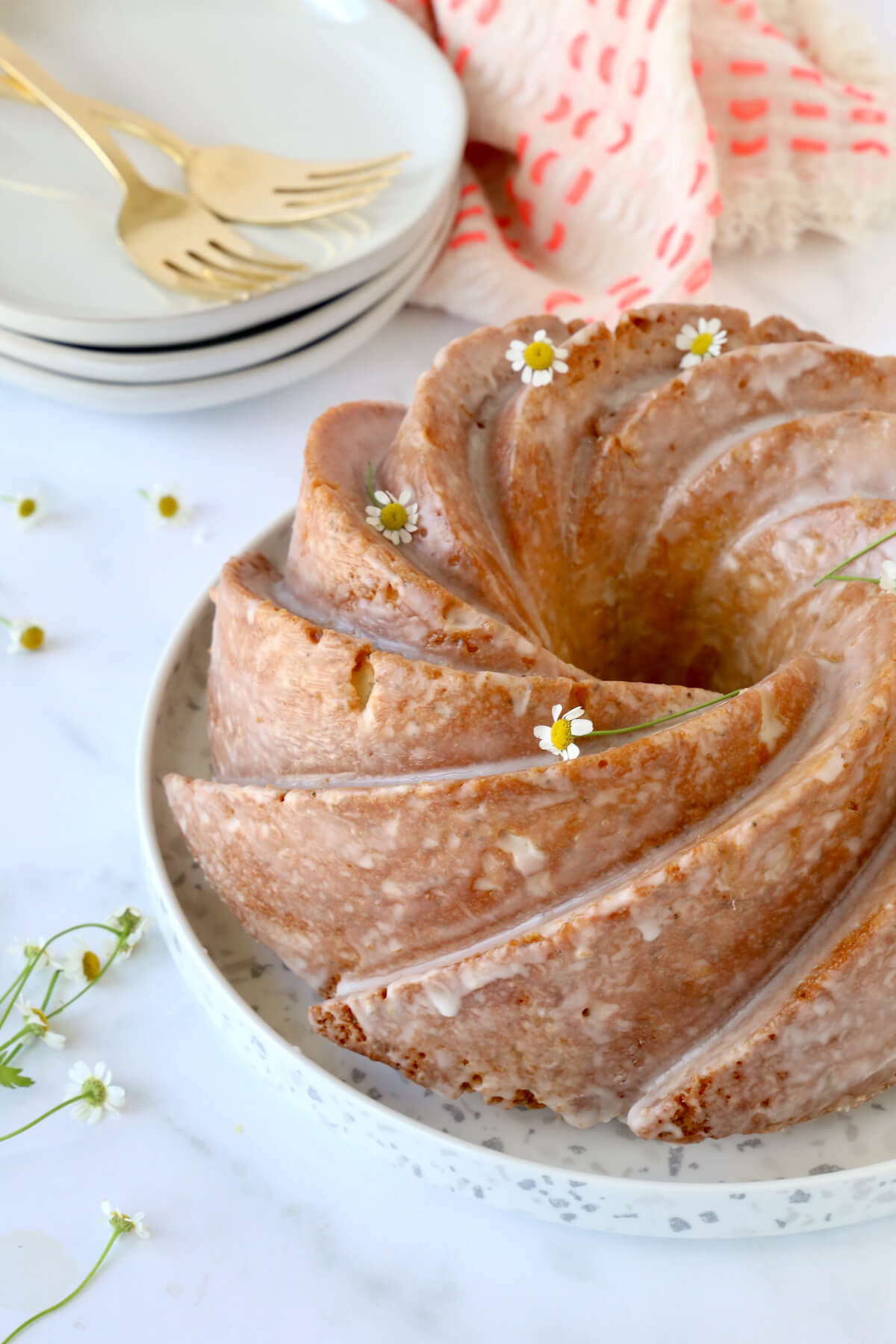 A nine inch bundt cake on a plate next to a stack of three dessert dishes and forks.  