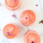 Four glass filled with a frothy pink drink with fresh flowers on top.
