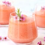 A glass filled with a frothy pink drink with fresh flowers on top.