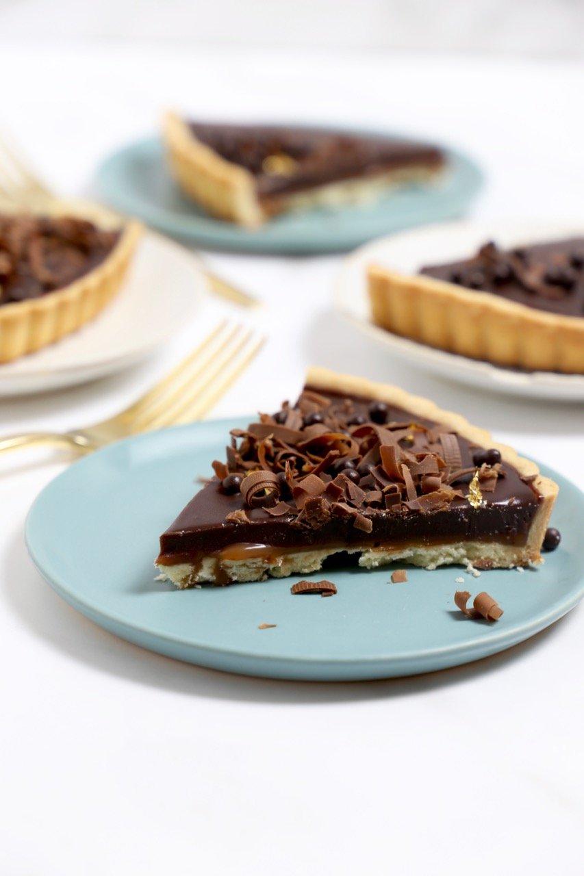 A slice of chocolate caramel tart on a plate next to a fork