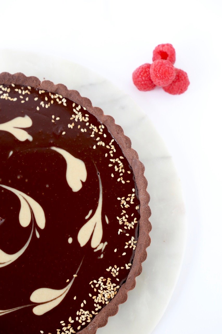 A close up image of a tart with chocolate crust, ganache filling and a tahini swirl 
