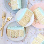 six slices of cake on different plates surrounded by rainbow sprinkles and two gold forks