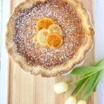 A wood board with a pie on top next to white tulips.