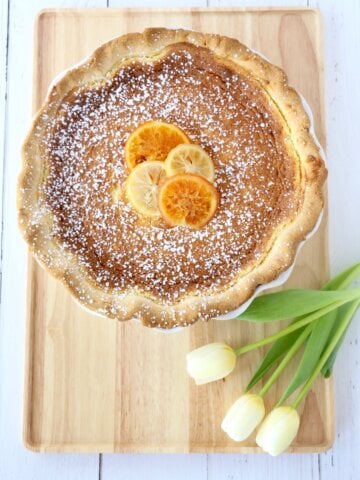 A wood board with a pie on top next to white tulips.