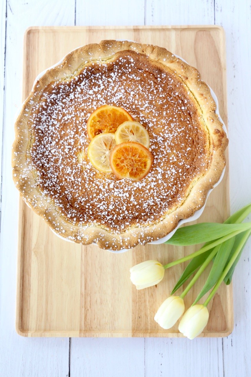 A wood board with a pie on top next to white tulips.  