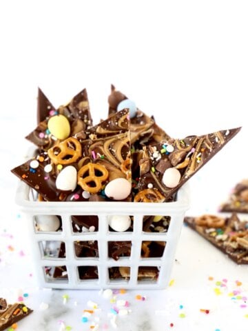 A white crate filled with chocolate bark topped with pretzels and malted easter eggs.