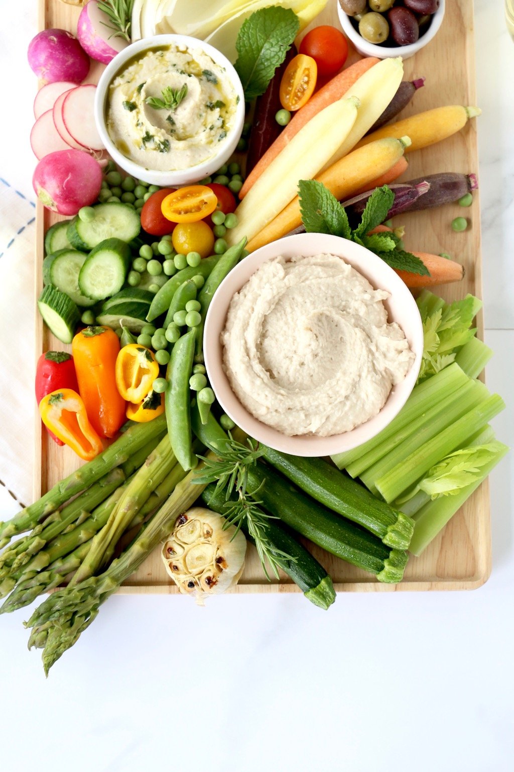 A wood board with fresh veggies and a bowl of white bean dip. 