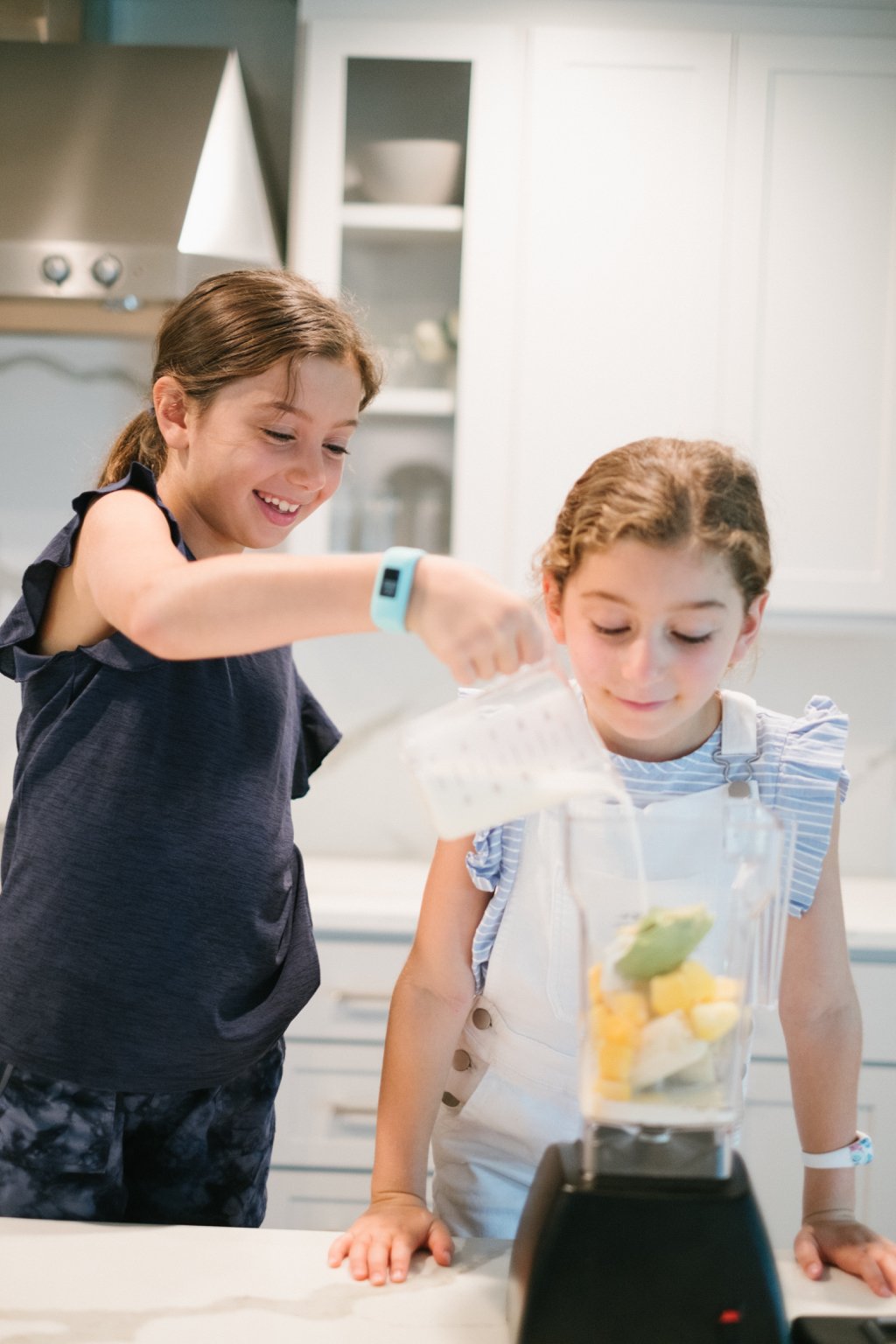 two girls, one pouring almond milk into a blender and the other watching