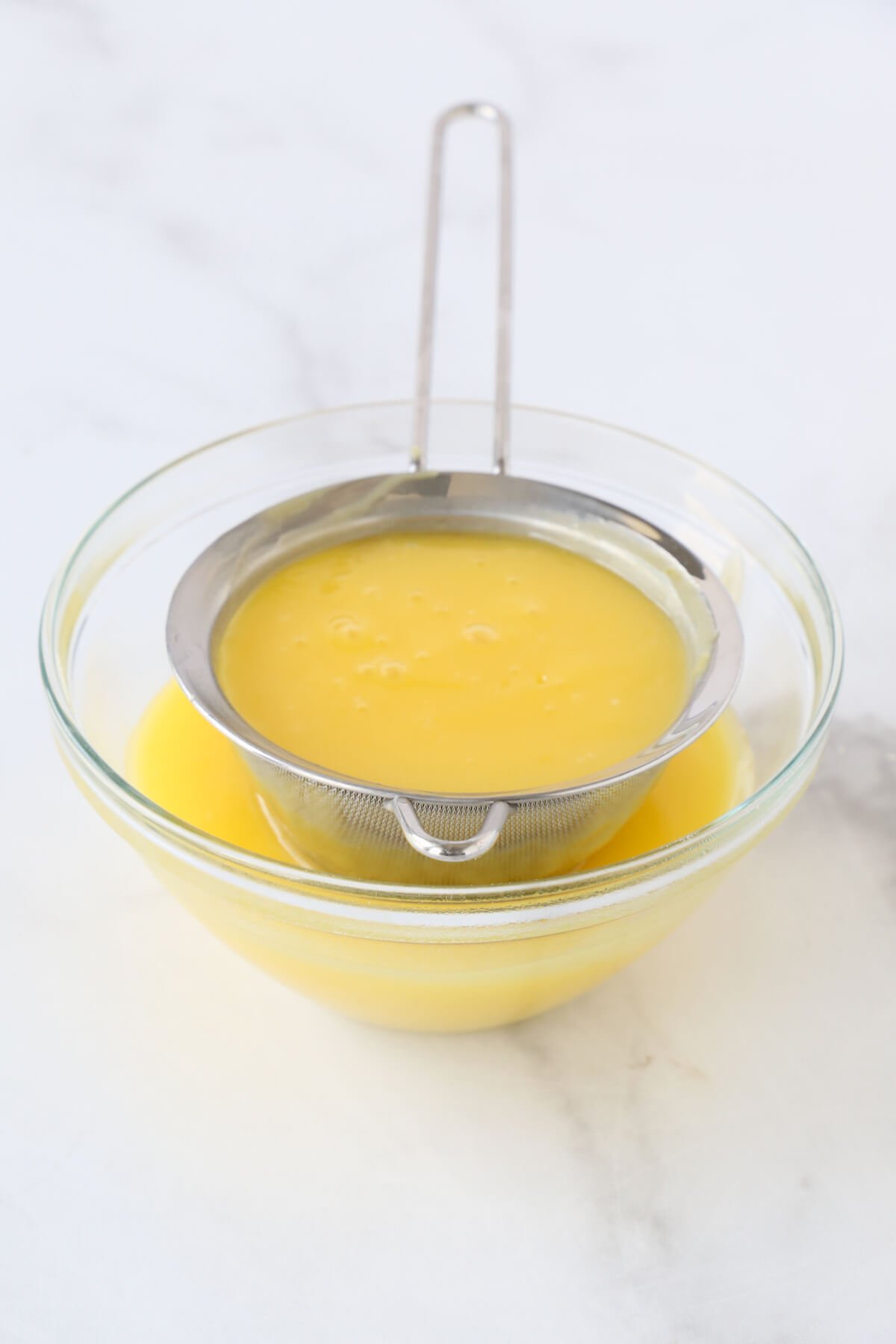 a glass bowl with lemon curd straining