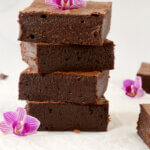 A stack of four brownies with purple flowers on top and next to them.