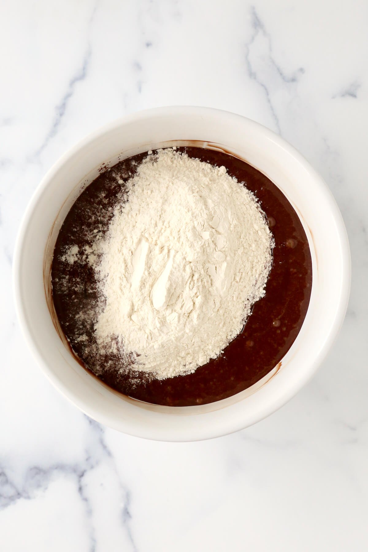 A bowl of chocolate batter with flour on top.  