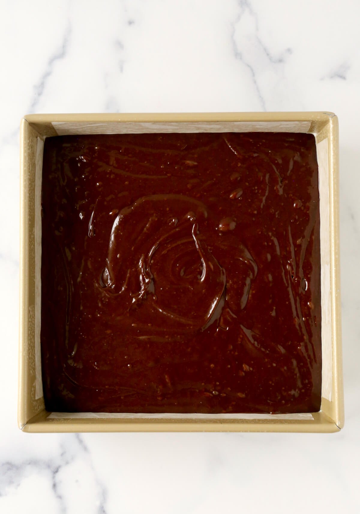 Chocolate brownie batter in a square gold pan. 