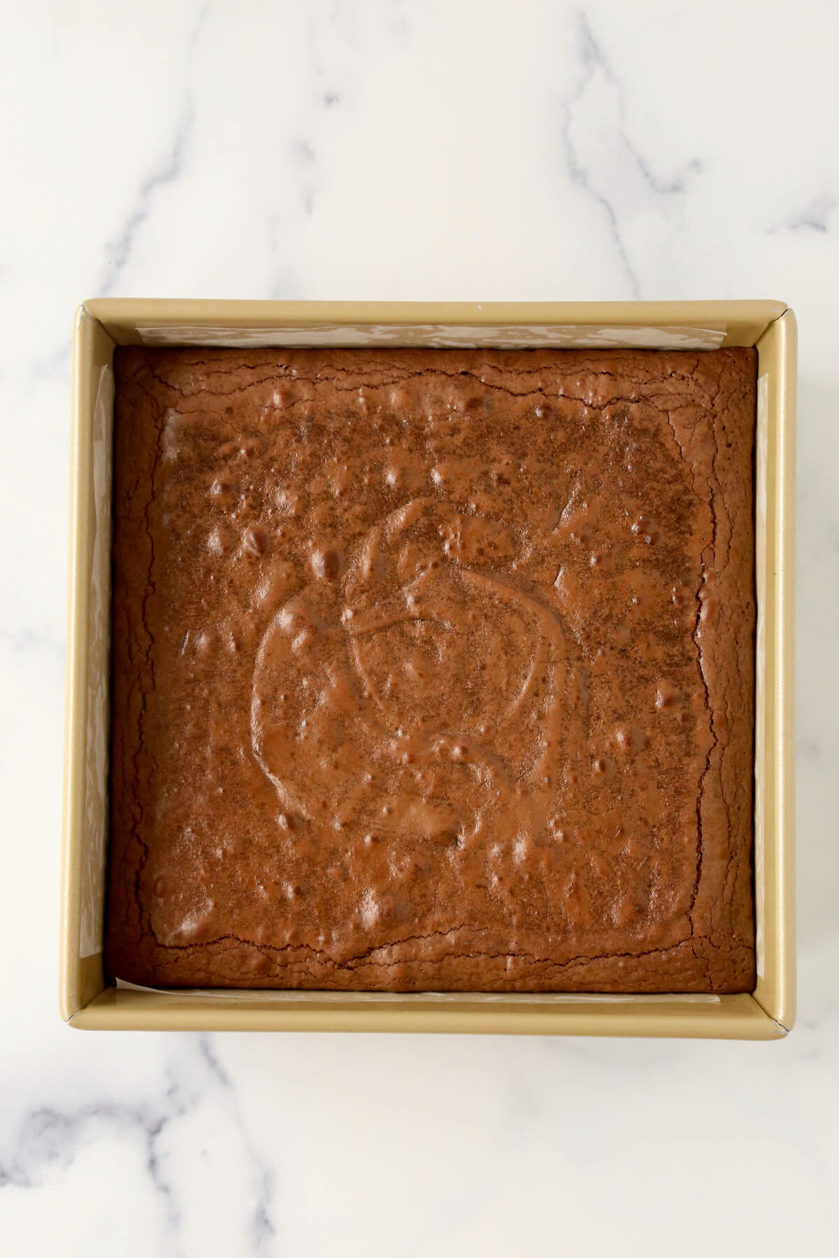 Chocolate brownie batter baked into a square gold pan.  