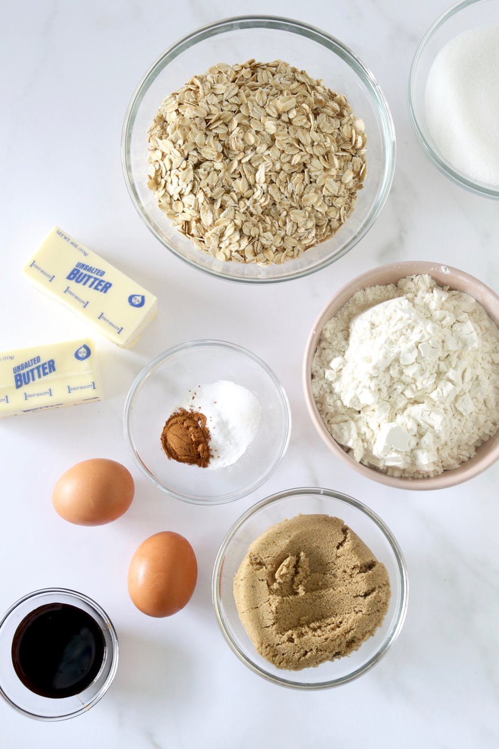 A bowl of oats, two sticks of butter,  a bowls of butter cream, two eggs, brown sugar, vanilla extract.  