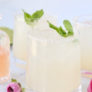 Three glasses with grapefruit, lime juice and tequila mixed together with a fresh mint leave on top next to pint flowers.