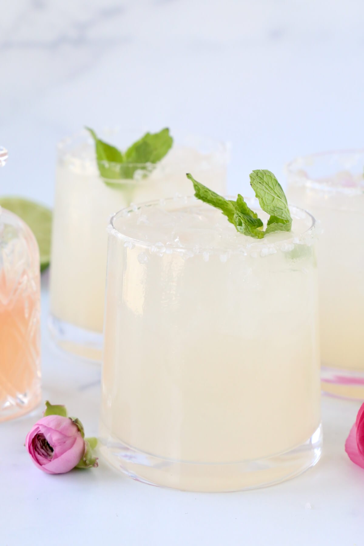 Three glasses with grapefruit, lime juice and tequila mixed together with a fresh mint leave on top next to pint flowers.
