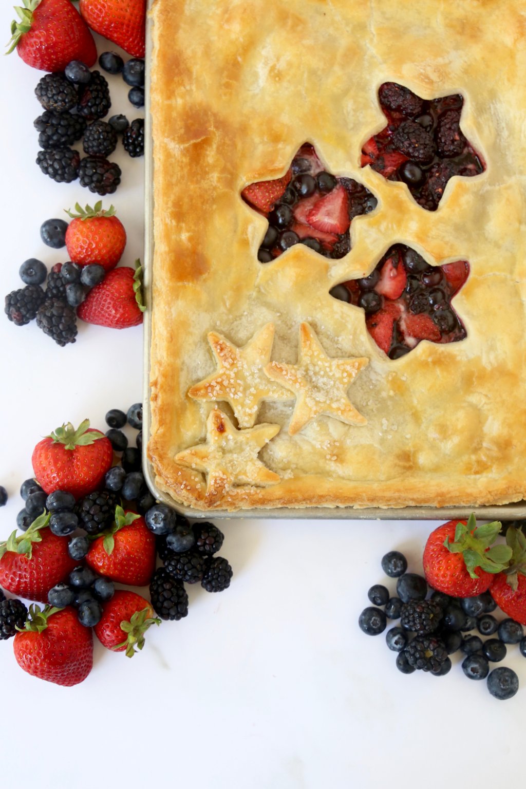 Strawberries, blueberries and blackberries piled next to a sheet pan with pie crust with star cut outs.  