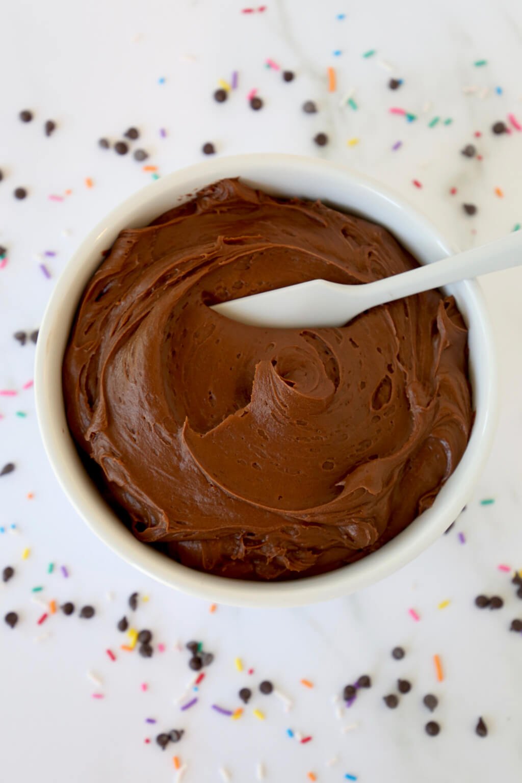 A bowl of chocolate buttercream frosting with a spoon in it