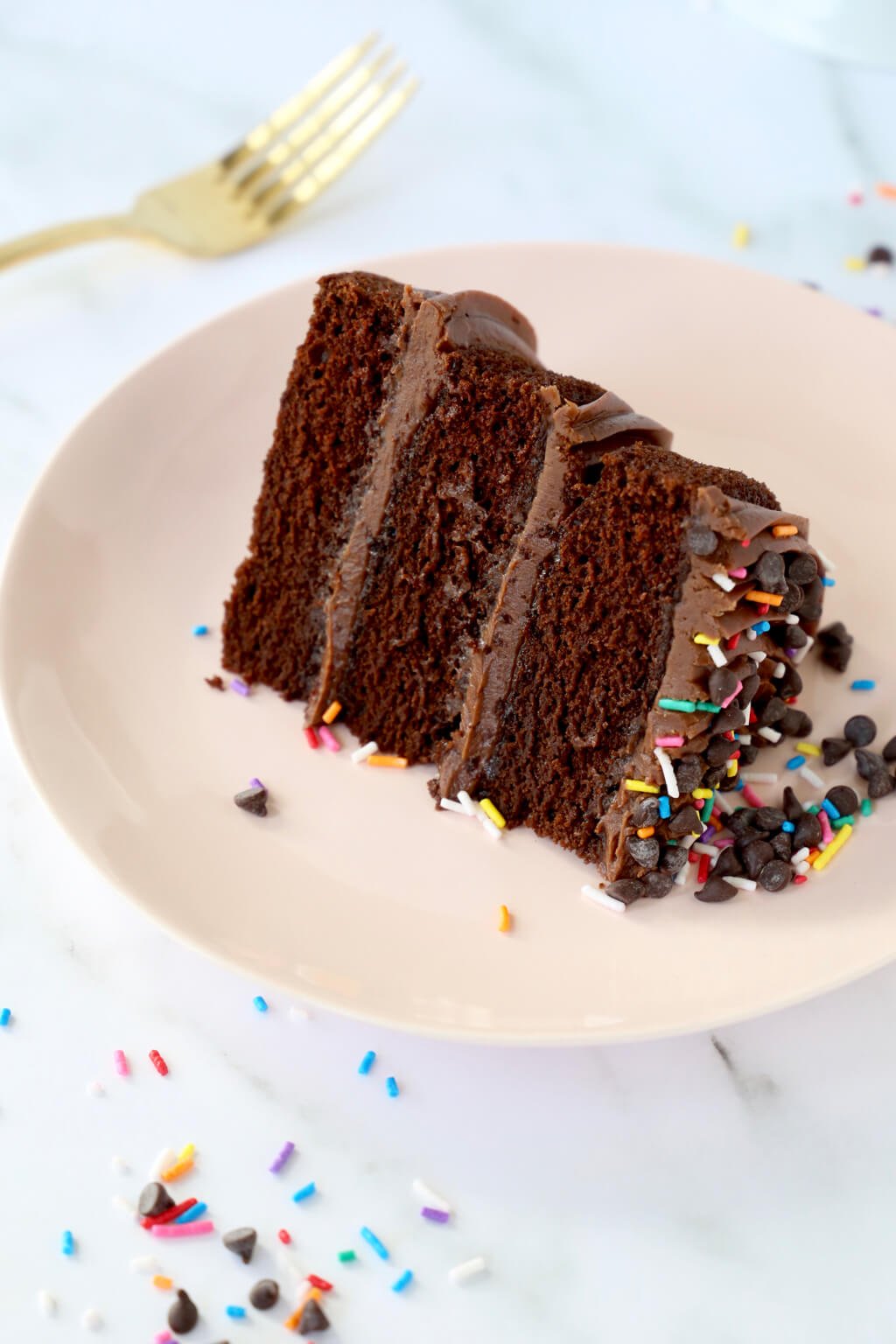 A slice of classic chocolate layer cake on a plate with a fork