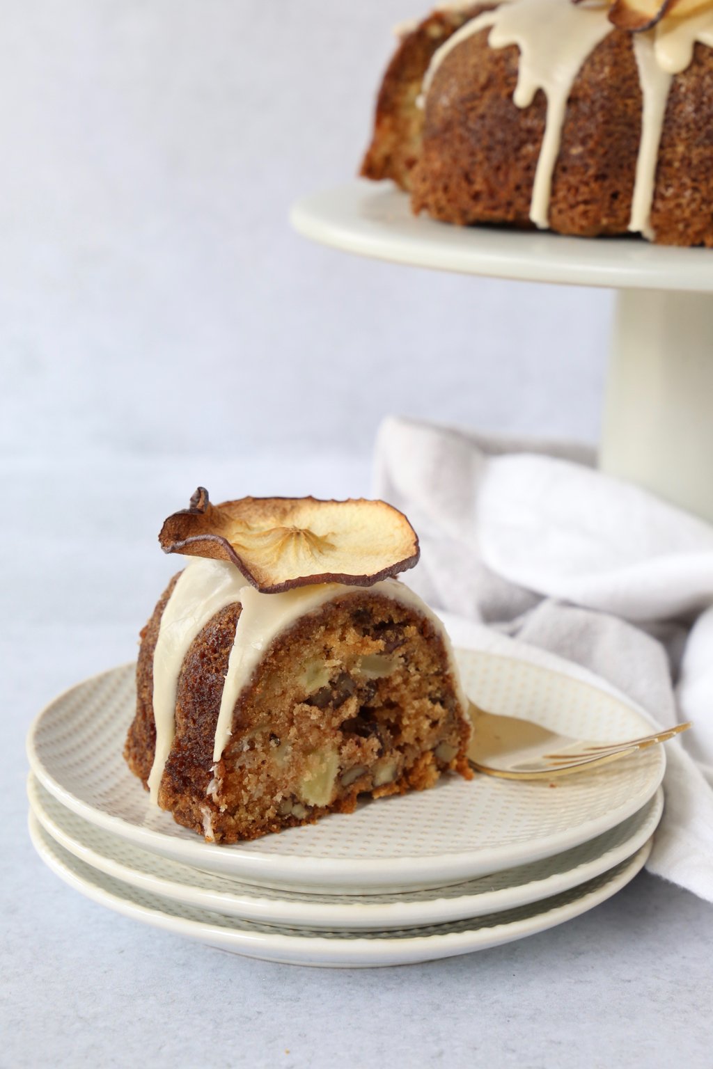 a slice of apple spice bundt cake on a stack of plates with the large bundt cake in the background 