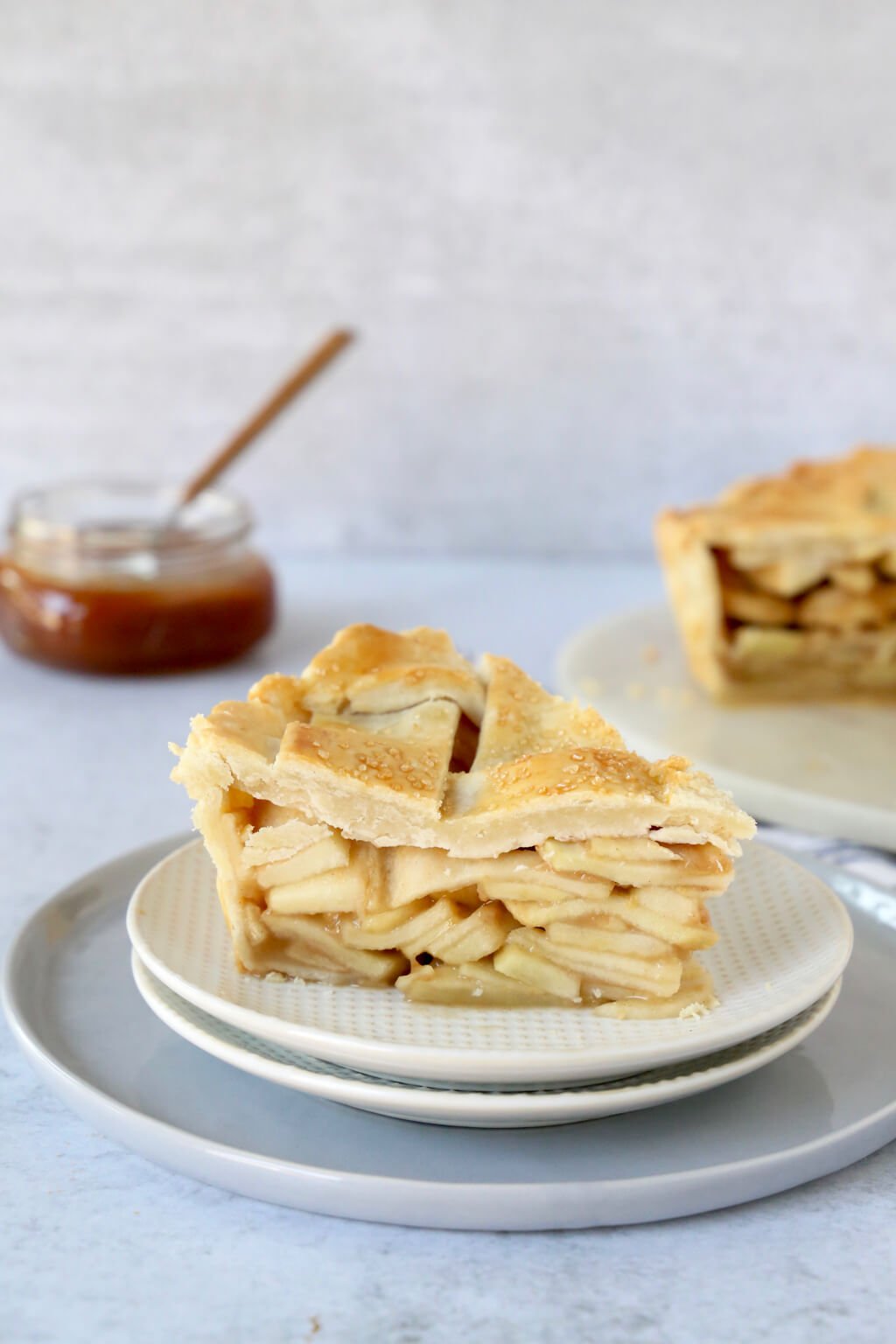 Slice of deep dish apple pie with caramel sauce in the background