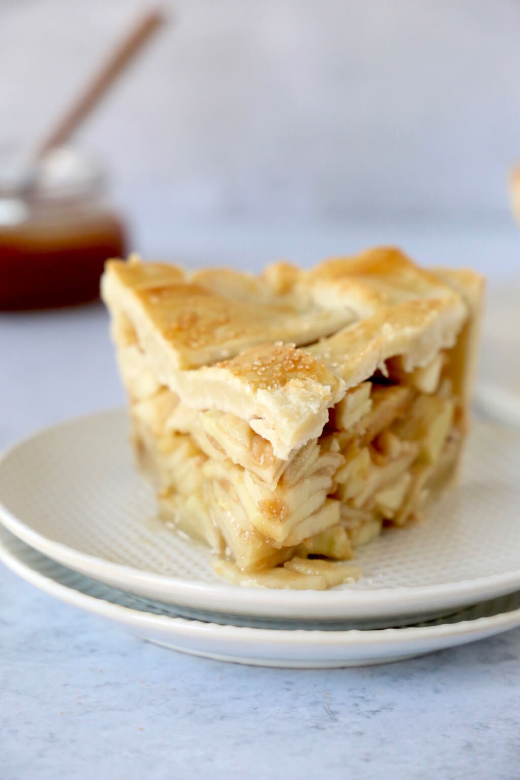 Slice of deep dish apple pie with caramel sauce in the background 