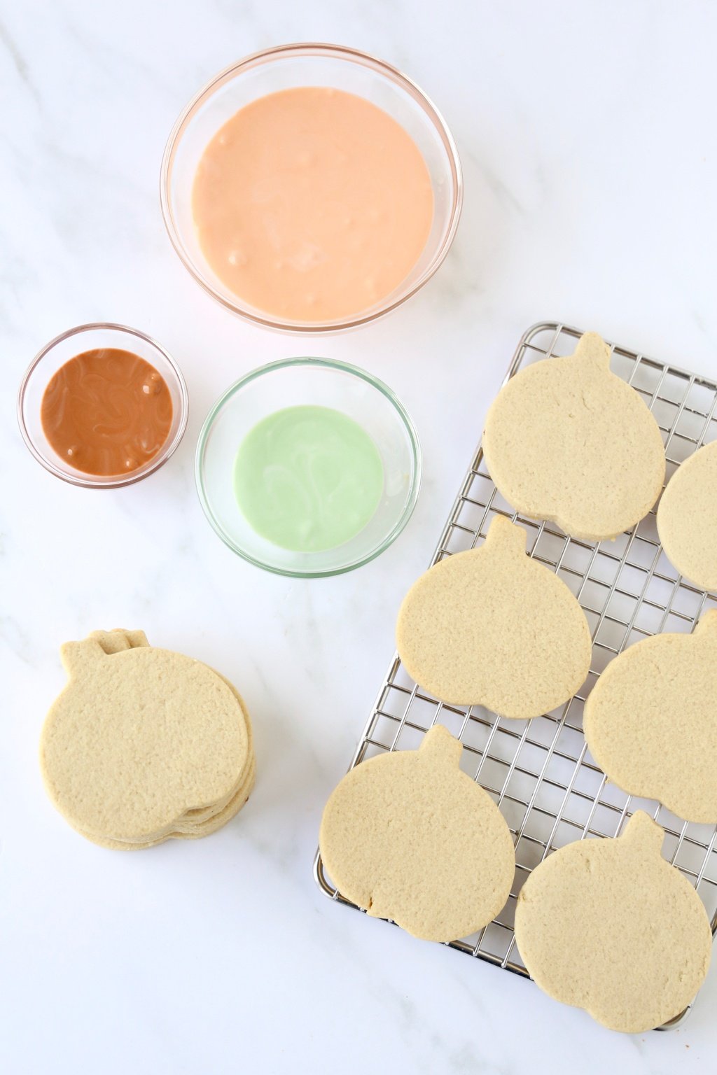 pumpkin shortbread cookies on a cooling rack with three bowls of icing