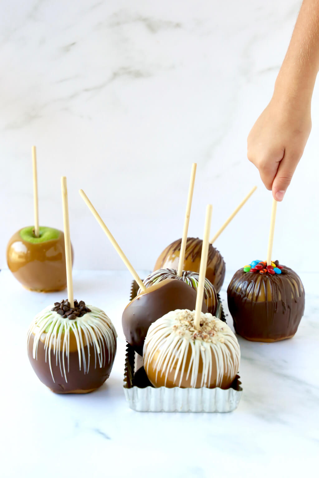 Caramel apples drizzled with chocolate, with a hand reaching in to grab one