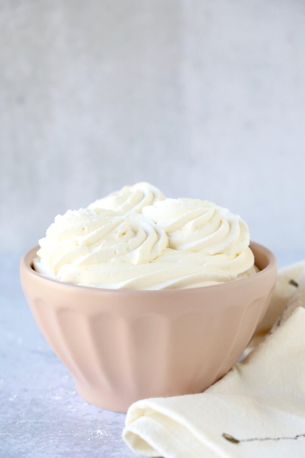 A pink bowl with white cream piped in swirls next to a towel. 