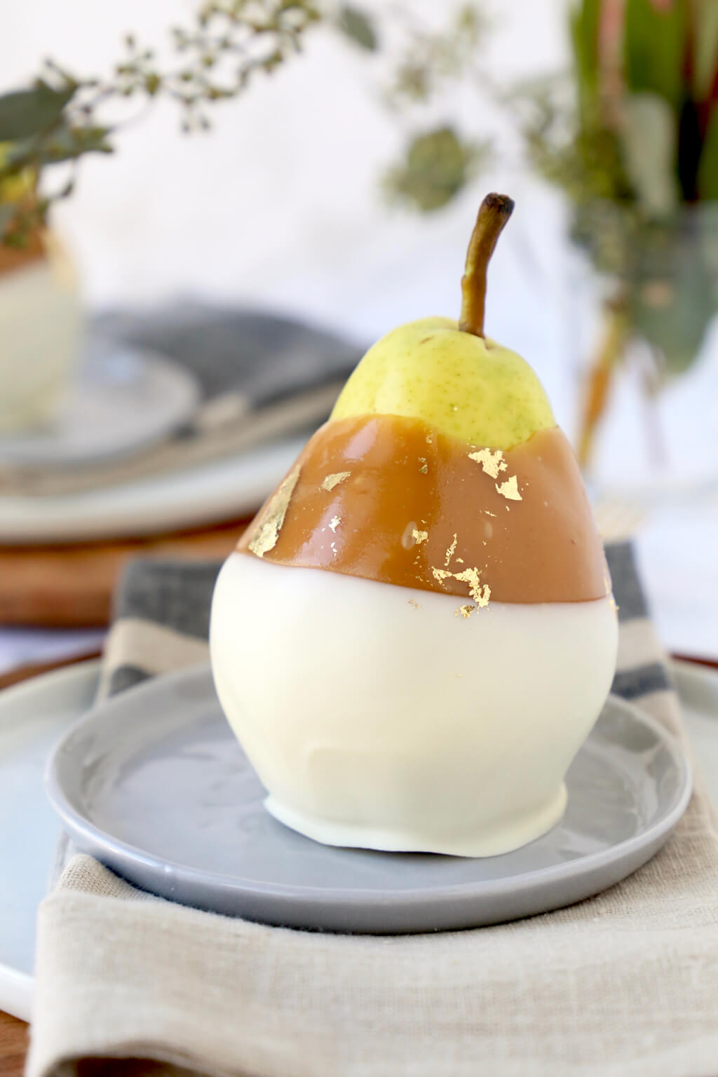 A gray small plate with a pear sitting on top dipped in light brown caramel and white chocolate.