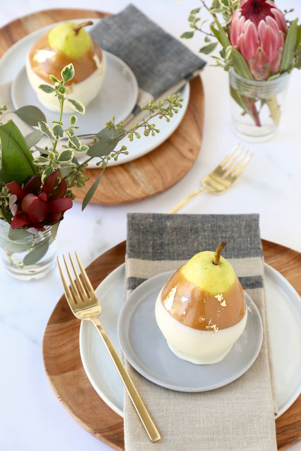 a table set with plates, napkins, forks, flowers and caramel pears 