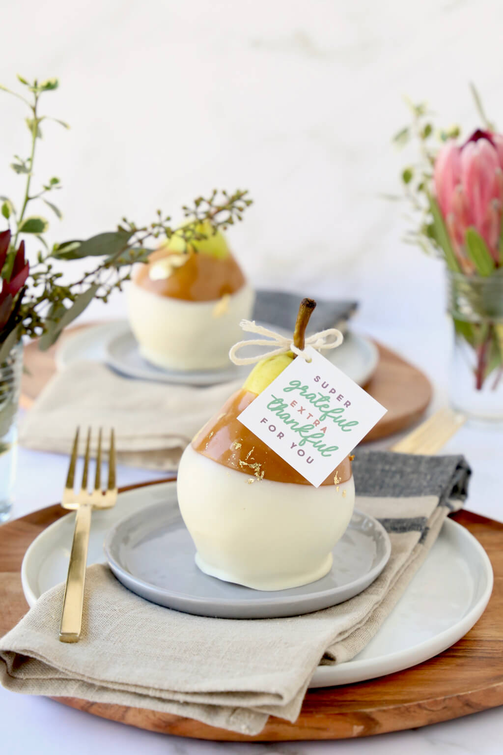 a table set with plates, napkins, fork, flowers and caramel pears with a tag