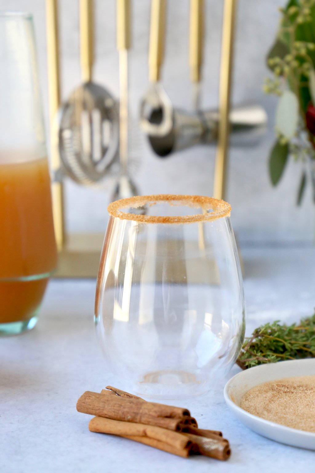 a clear glass with cinnamon sugar on the rim surrounded by ingredients and barware