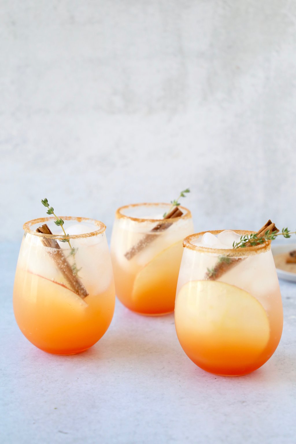 three glasses of a red orange colored cocktail with a cinnamon stick and thyme leave in each glass