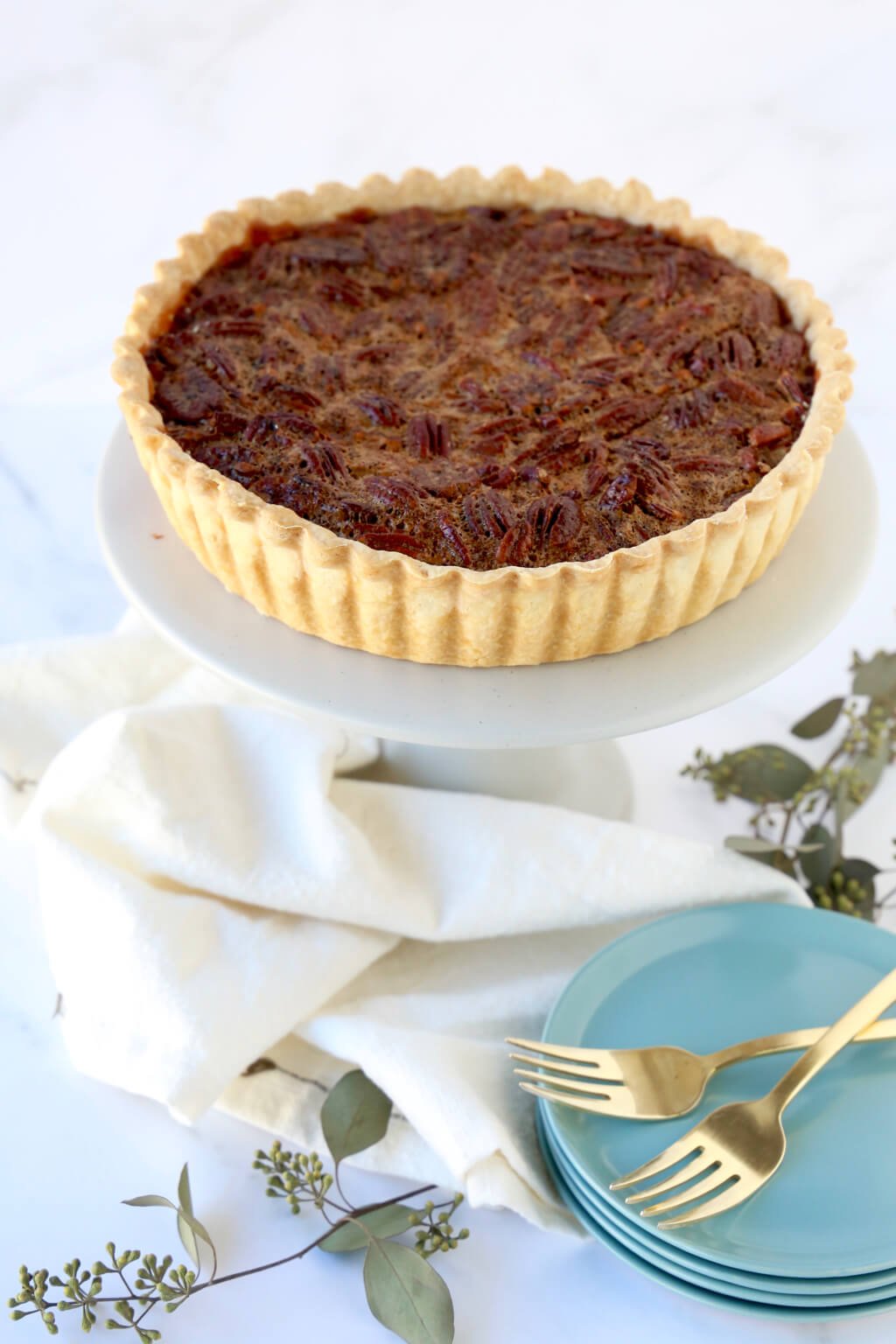 deep dish chocolate pecan tart on a cake stand, with a stack of plates and forks below it