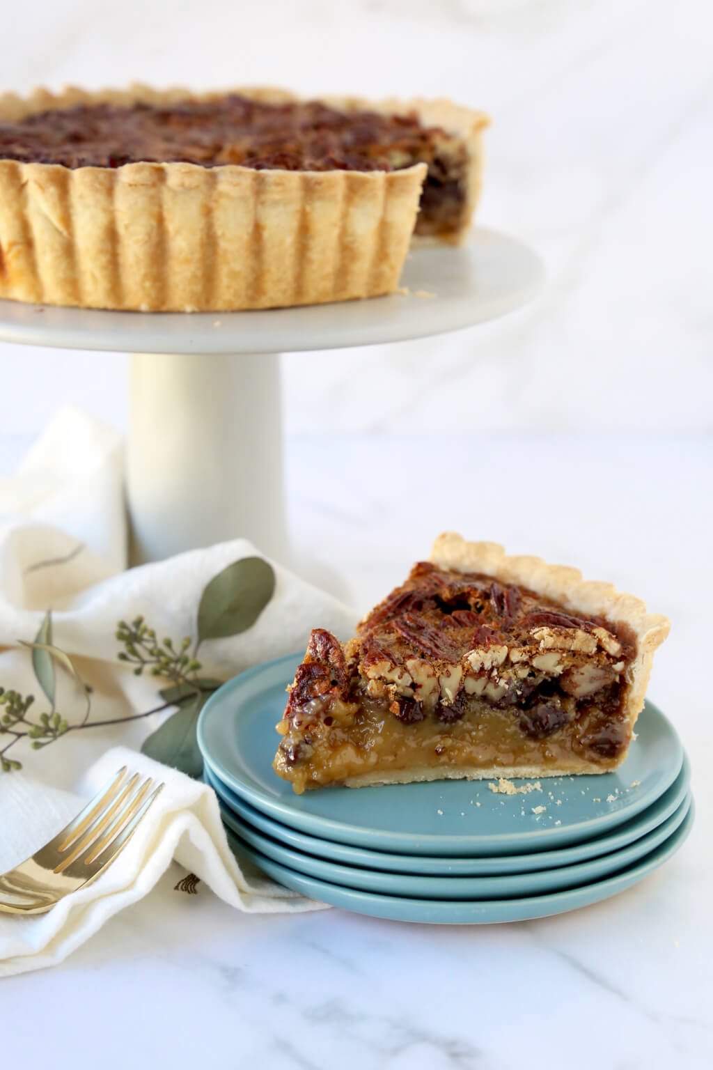 a slice of pecan tart on a stack of dishes and the full tart behind it 