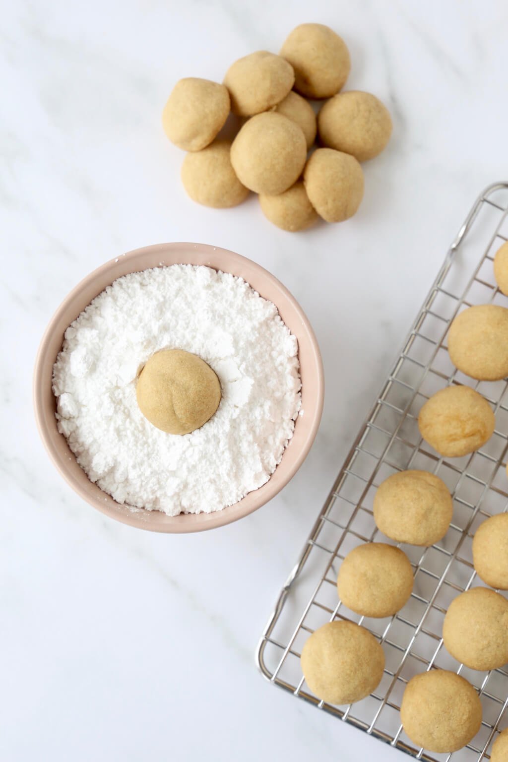 One cookie in a bowl of powdered sugar showing how to coat the cookie after it is baked