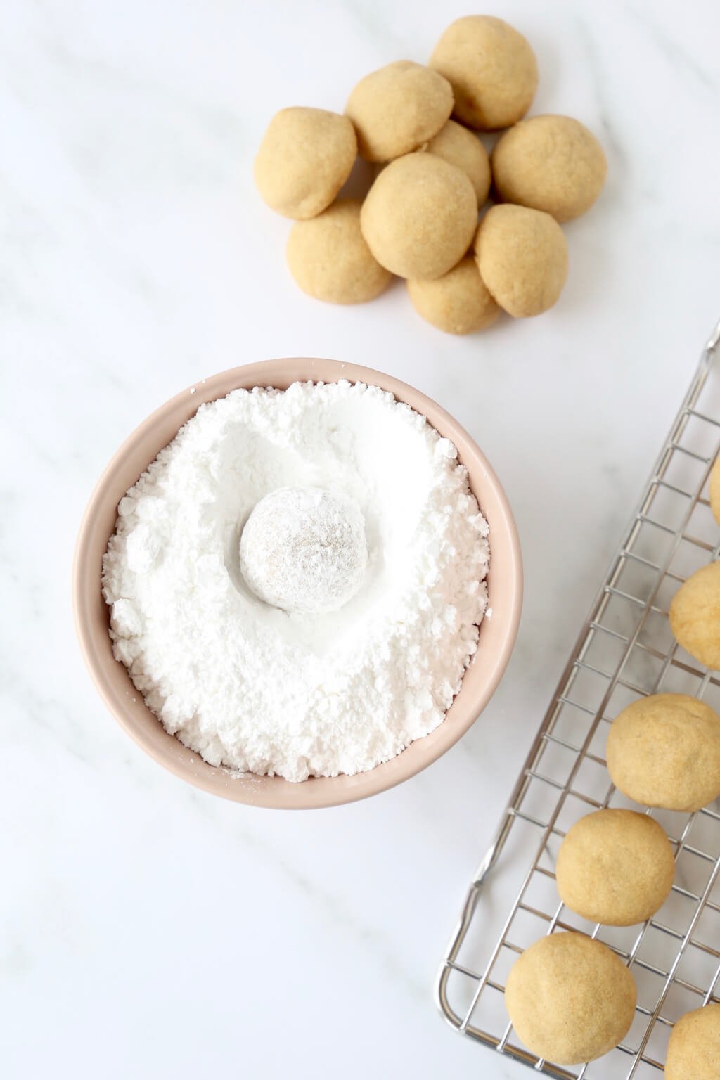 One cookie in a bowl of powdered sugar showing how to coat the cookie after it is baked 