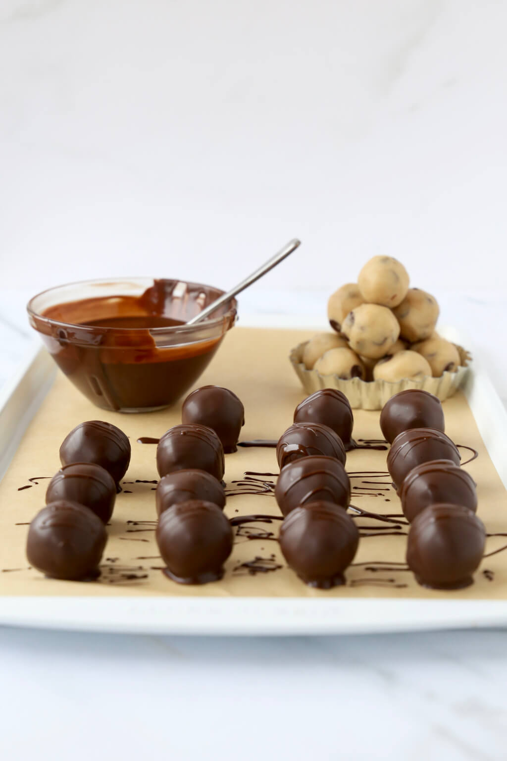 A tray of chocolate chip cookie dough balls that have just been dipped in chocolate glaze