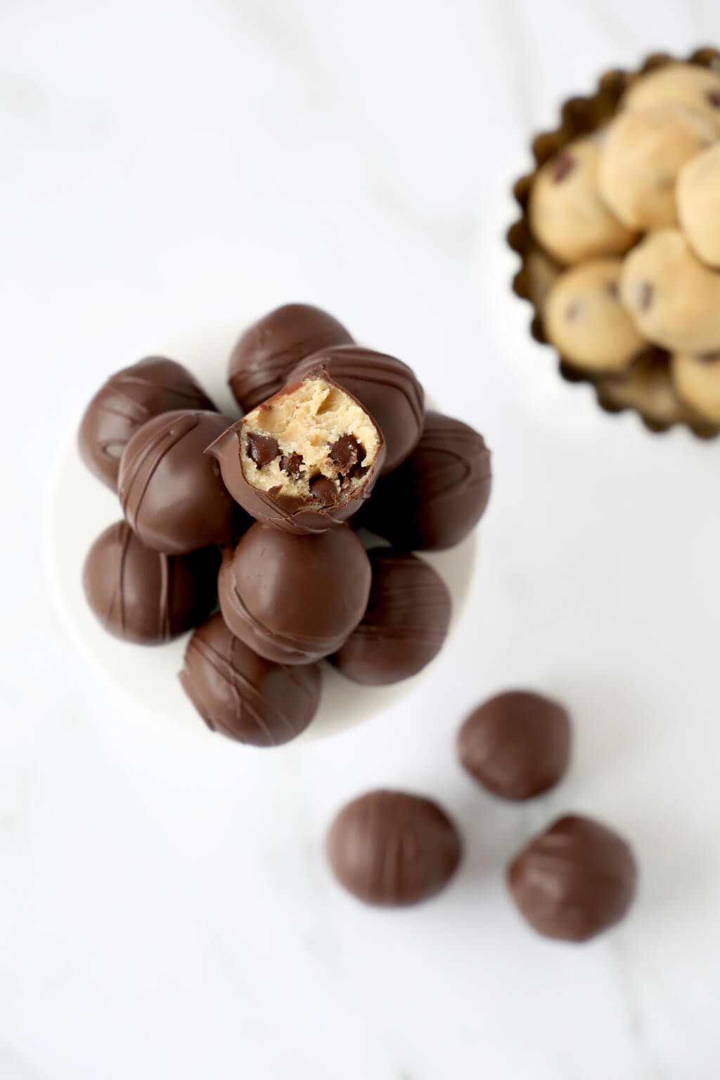 A pile of chocolate cookie dough balls. The very top one has a bite taken out so the cookie dough center is visible.