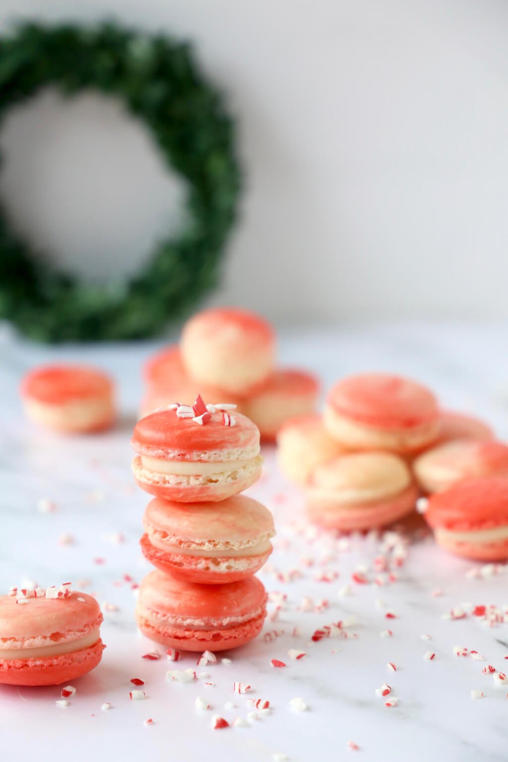 three peppermint white chocolate french macarons stacked on top of each other, with more macarons in the background