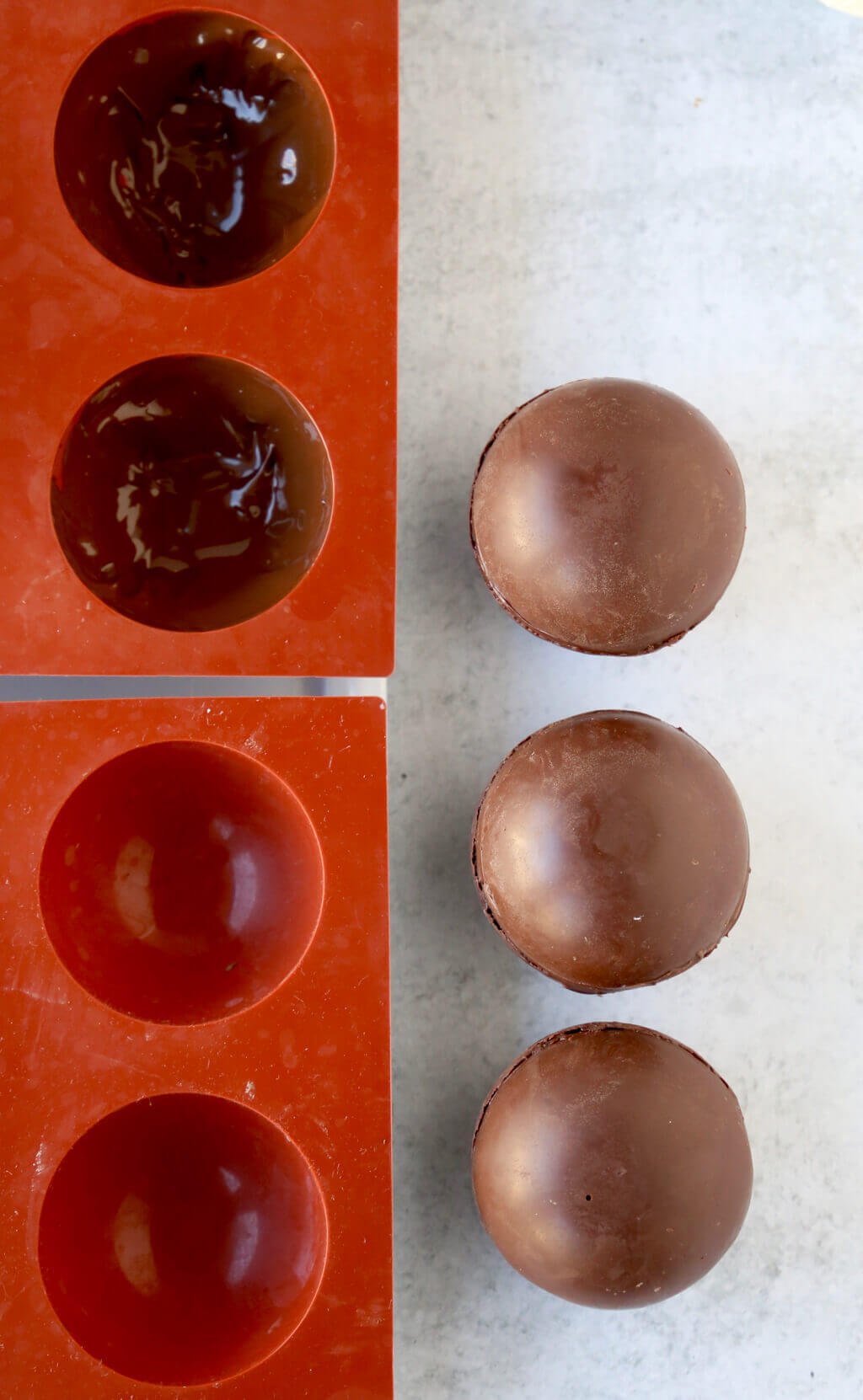Dome molds covered in melted chocolate next to hardened chocolate domes that have just come out of the molds